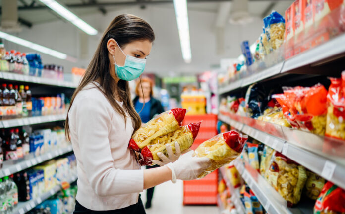 Buyer wearing a protective mask.Shopping during the pandemic quarantine.Nonperishable smart purchased household pantry groceries preparation.Woman buying few pasta packages.Budget pastas and noodles.