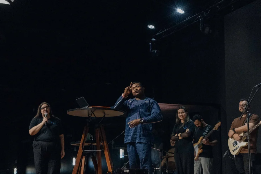 Pastores surdos em um palco na Abba Pai Church, ministrando a Palavra em Libras, com a plateia composta por pessoas surdas e ouvintes ao fundo.