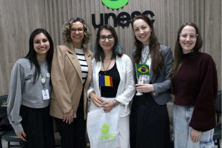 A acadêmica romena Ioana-Catalina Caraveteanu sendo recebida pela pró-reitora Vanessa Moraes de Andrade e a assessora Cinara Ludvig Gonçalves na Unesc.