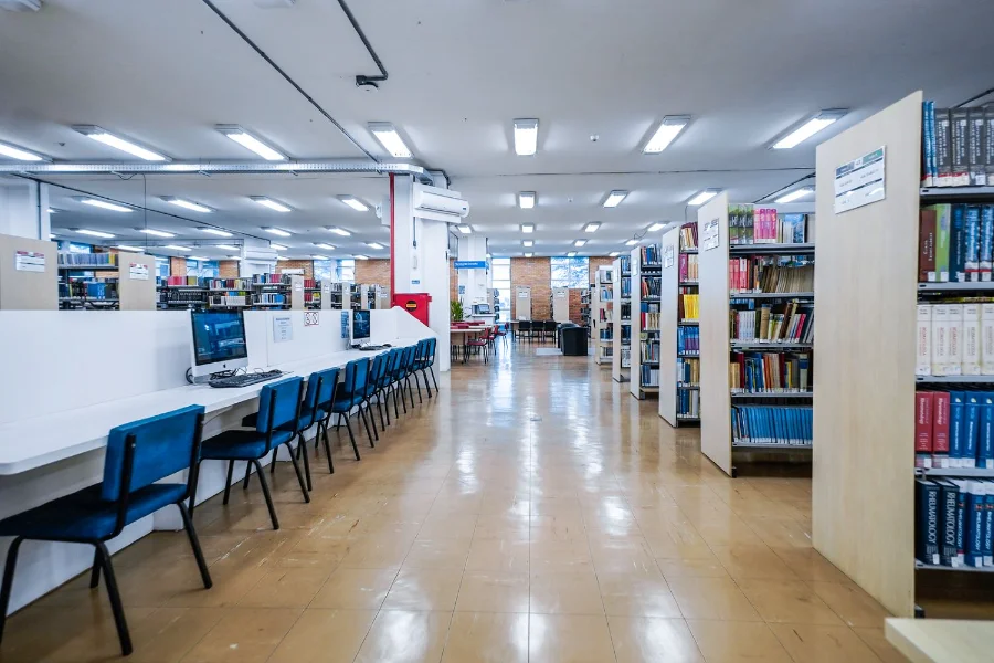 Uma ilustração de uma moderna biblioteca universitária, com estudantes engajados em leitura e pesquisa entre as estantes, simbolizando o acesso e a permanência no ensino superior promovidos pelo programa Universidade Gratuita.