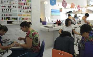 Anvisa proíbe duas substâncias cancerígenas em esmalte em gel Manicure aplicando esmalte em gel em uma cliente em um salão de beleza, representando os profissionais afetados pela proibição de substâncias cancerígenas em produtos de unhas pela Anvisa.