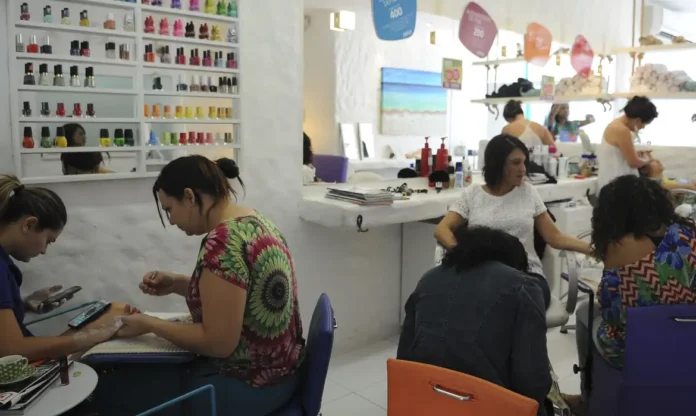 Anvisa proíbe duas substâncias cancerígenas em esmalte em gel Manicure aplicando esmalte em gel em uma cliente em um salão de beleza, representando os profissionais afetados pela proibição de substâncias cancerígenas em produtos de unhas pela Anvisa.