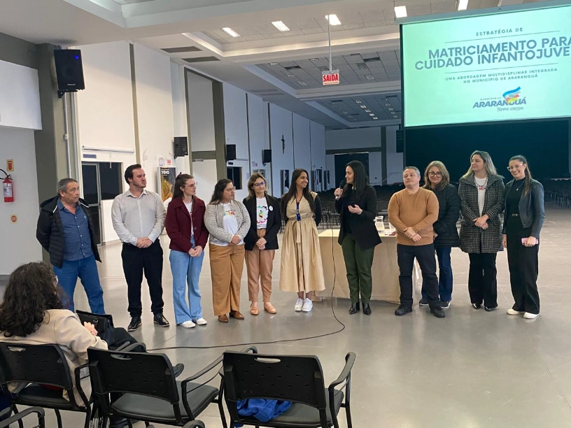 Araranguá se capacita para avaliação de TEA em Turvo Equipe de saúde e educação de Araranguá apresentando o Projeto de Matriciamento Infantojuvenil em um palco, durante a capacitação sobre Transtorno do Espectro Autista (TEA) realizada em Turvo.