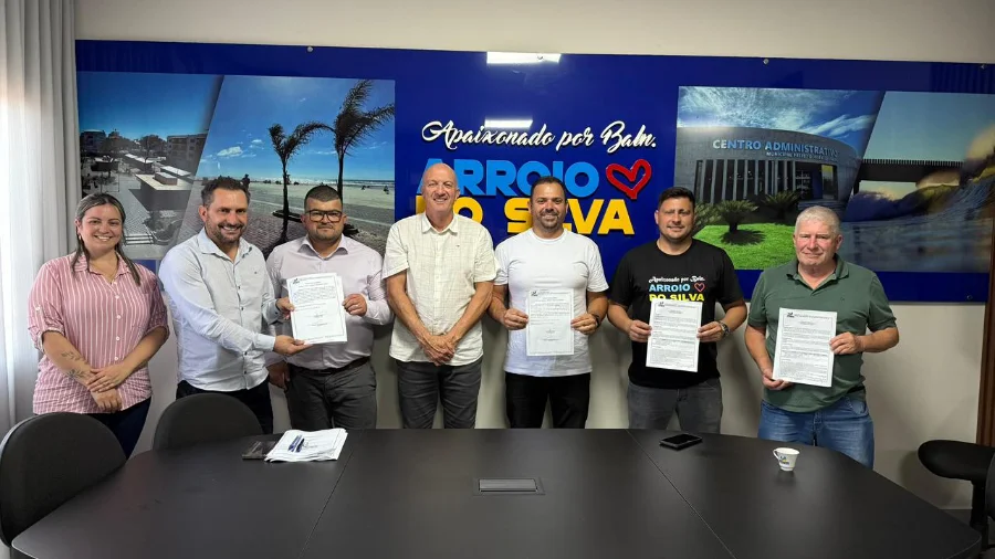 O prefeito Evandro Scaini e outras autoridades em uma mesa, assinando as ordens de serviço para a pavimentação da Rua João Manoel Coelho e o novo Parque Farroupilha.