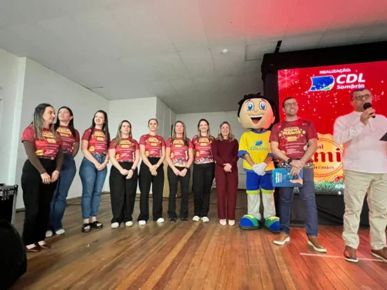 Equipe feminina da CDL Sombrio no palco, ao lado do mascote CDLinho e do locutor, em evento de capacitação focado em vendas.