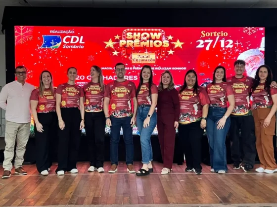 Grupo de organizadores do evento da CDL Sombrio no palco, em frente ao painel do 'Show de Prêmios', celebrando a capacitação do comércio local.