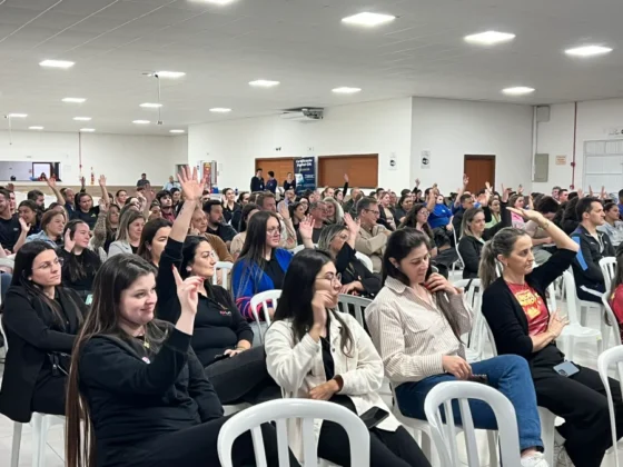 Plateia lotada de comerciantes e empresários no evento de capacitação da CDL Sombrio, com muitas pessoas levantando as mãos em resposta à interação do palestrante.