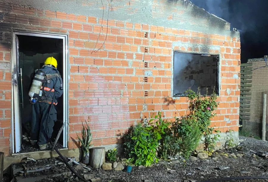 Bombeiro entra em casa de tijolos com fachada danificada e queimada, após ser totalmente destruída por incêndio em Praia Grande.