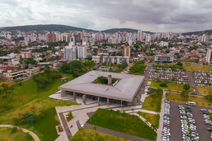 Criciúma Dia do Servidor altera Saúde e Educação Vista aérea do Paço Municipal de Criciúma, com o prédio de arquitetura marcante em primeiro plano e a área urbana ao fundo, em contexto de alteração nos serviços de Saúde e Educação no Dia do Servidor.