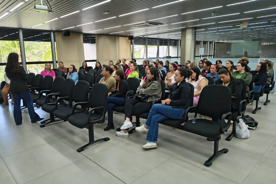 Palestrante em pé em frente a um auditório lotado de professoras e educadoras em Criciúma, durante o evento de formação para o Dia do Professor.