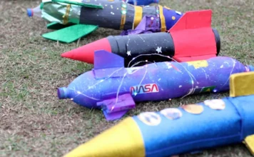 Criciúma promove competição de foguetes sobre o Centenário Foguetes artesanais feitos de garrafas PET, decorados com cores vibrantes e brilho, deitados na grama e prontos para a Competição Interclubes de Foguetes em Criciúma.