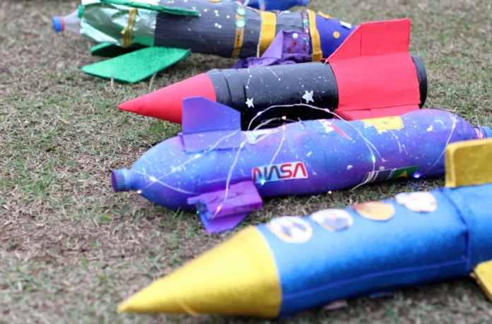Criciúma realizará 4ª Competição Interclubes de Foguetes 1 Foguetes artesanais feitos de garrafas PET, decorados com cores vibrantes e brilho, deitados na grama e prontos para a Competição Interclubes de Foguetes em Criciúma.