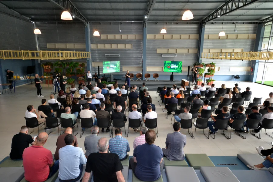 Vista do público em um galpão moderno em Criciúma, assistindo a palestrantes no palco do evento CRIO Conecta Summit de tecnologia e inovação.