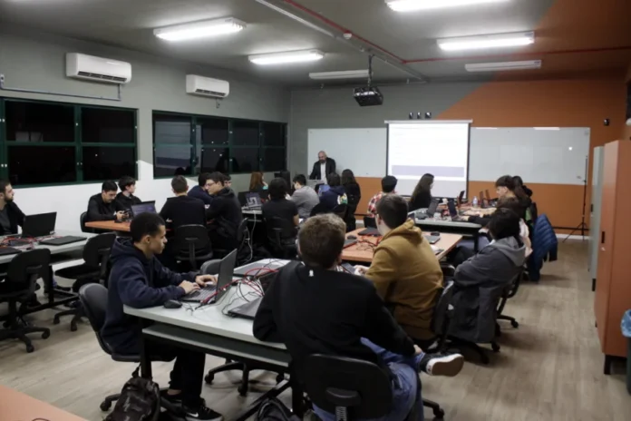 Dia do Professor Unesc destaca o papel central na formação Professor palestrando em sala de aula na UNESC (Criciúma) para alunos usando notebooks, destacando o papel central do docente na formação profissional.