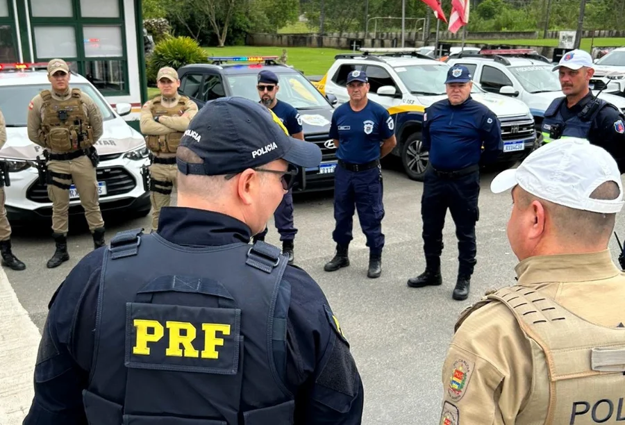 Policiais de diversas corporações, incluindo PRF (Polícia Rodoviária Federal), Polícia Militar e Polícia Civil, reunidos para briefing em frente às viaturas, em ação de segurança conjunta para as Festas de Outubro.