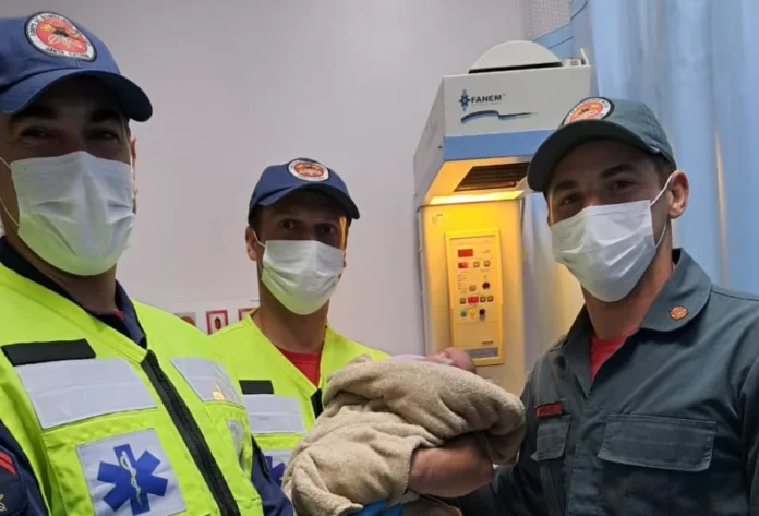 Forquilhinha Bebê nasce em casa com auxílio de bombeiros Três bombeiros de Forquilhinha, vestindo máscaras e uniformes, sorriem enquanto seguram um recém-nascido envolvido em uma manta, após auxiliar o parto em casa.