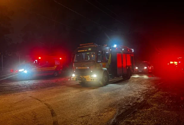 Caminhão de resgate e ambulância do Corpo de Bombeiros com luzes de emergência acesas, na estrada escura, mobilizados para o resgate do carro que caiu no rio em Forquilhinha.
