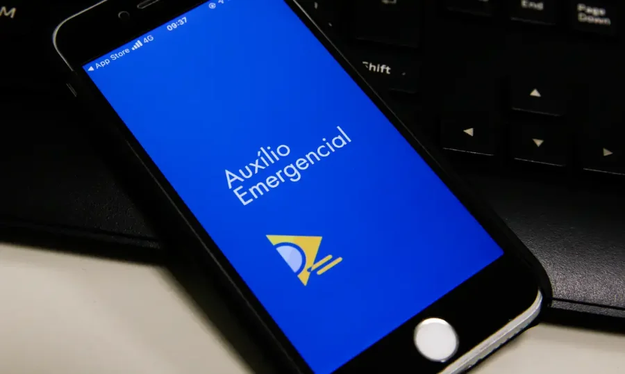Tela de smartphone com o aplicativo Auxílio Emergencial, ilustrando o tema de pagamentos ou cobranças indevidas.