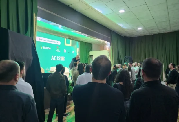 Palestrante Pedro Reis no palco com luz verde em frente a uma plateia lotada no IV Fórum Empresarial da ACIS em Sombrio, debatendo temas de mercado.