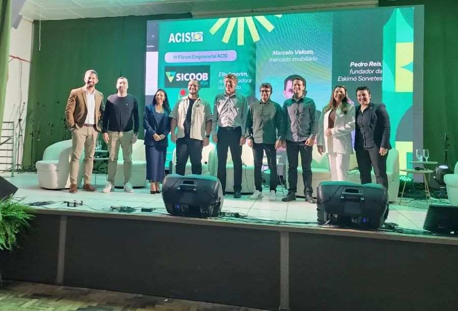 IV Fórum Empresarial ACIS 2025 reúne empresários em Sombrio Painel de convidados e palestrantes no palco, com a logo da ACIS e informações sobre SICOOB e UNESC, durante o IV Fórum Empresarial em Sombrio.