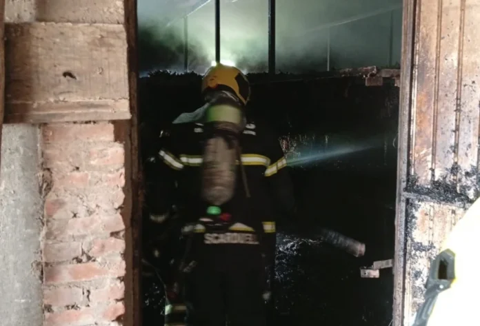 Incêndio atinge estufa de fumo em São João do Sul Bombeiro com capacete e equipamento de respiração entrando em estufa de fumo em chamas em São João do Sul, com fumaça escura ao fundo.