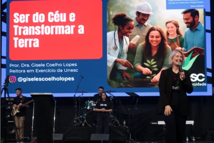 Juventude Reitora da Unesc destaca formação e coragem Reitora Gisele Coelho Lopes, da UNESC, discursando em palco com microfone, em evento para jovens, destacando a importância da formação e da coragem para "Transformar a Terra".