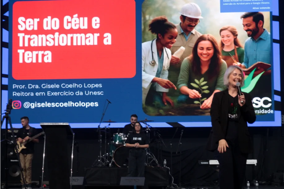 Reitora Gisele Coelho Lopes, da UNESC, discursando em palco com microfone, em evento para jovens, destacando a importância da formação e da coragem para 