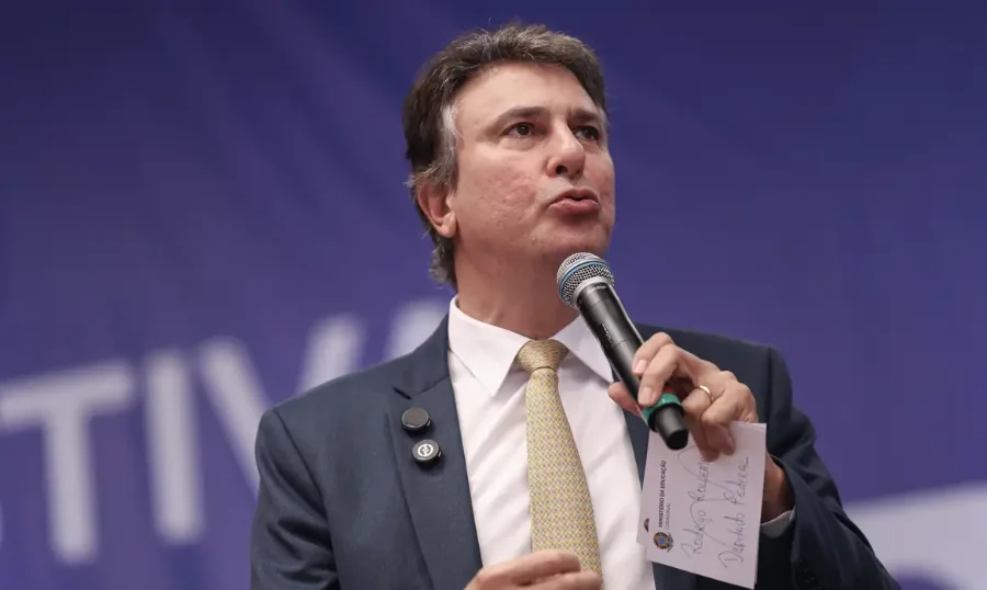 Ministro da Educação Camilo Santana discursando em um evento, com microfone em mãos, defendendo o salário digno para professores no Dia do Professor.