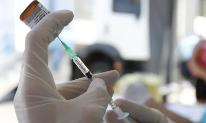 Multivacinação - crianças e jovens podem se vacinar (1) Um enfermeiro em um posto de saúde, com máscara e luvas, preenchendo uma seringa com líquido de uma ampola, preparando a vacina para a campanha nacional de multivacinação.