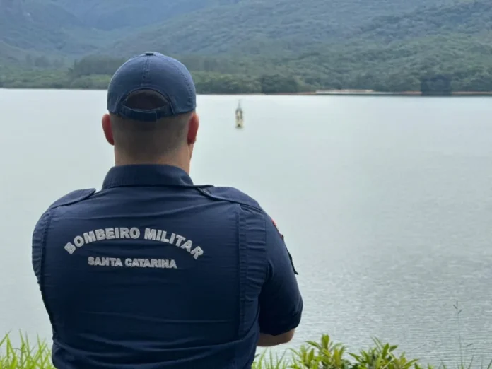 Nova Veneza Bombeiros buscam fugitivo de clínica com drone Bombeiro Militar de Santa Catarina de costas, olhando para um lago em Nova Veneza, durante a operação de busca a um fugitivo de clínica, com apoio de drone.
