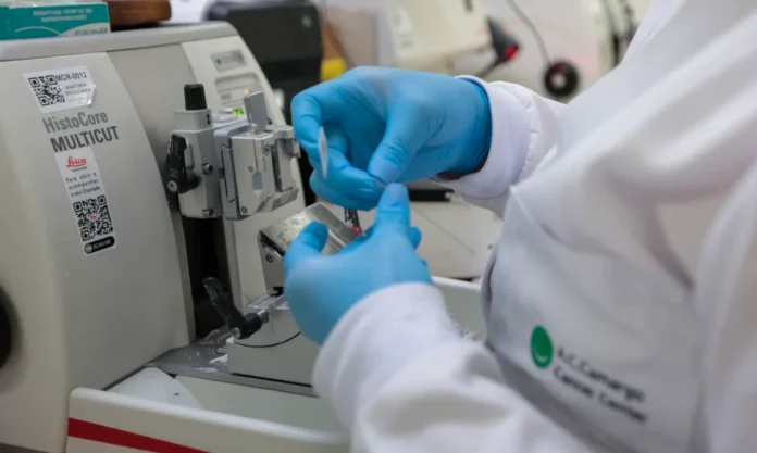 Novembro Azul Cura do câncer de próstata pode atingir 98% Profissional de laboratório com luvas azuis manuseando amostras em um micrótomo (equipamento de análise de tecido), ilustrando a pesquisa e o tratamento do câncer de próstata no Novembro Azul.