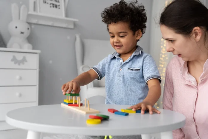 Novo decreto cria Política Nacional de Educação Inclusiva Criança sorridente brinca com um quebra-cabeça de encaixe na mesa, ao lado de uma professora ou cuidadora, ilustrando o foco da nova Política Nacional de Educação Inclusiva.
