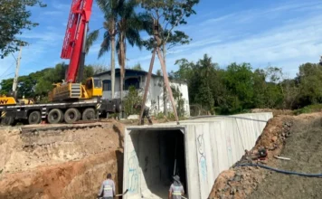 Obras de drenagem avançam contra alagamentos em Araranguá Guindaste vermelho e amarelo instalando uma grande peça pré-moldada de concreto para a obra de drenagem em Araranguá.