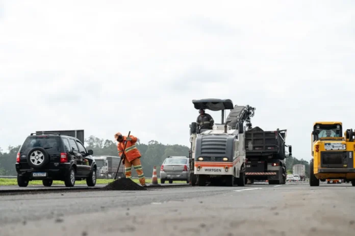 Obras na BR-101 terão interdição parcial de faixas marginais Trabalhadores e máquina pavimentadora (Wirtgen) em obra de recapeamento na BR-101, com interdição parcial das faixas marginais e carros passando ao lado.