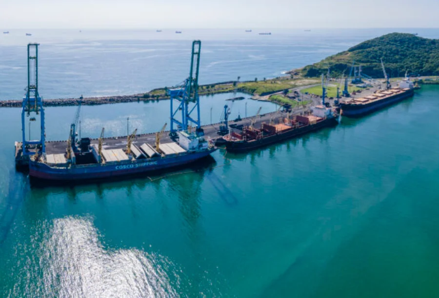 Porto de Imbituba movimenta 5,4 mi de toneladas Vista aérea do Porto de Imbituba com guindastes e navios de carga atracados, simbolizando a movimentação de 5,4 milhões de toneladas e a força do comércio exterior em Santa Catarina.