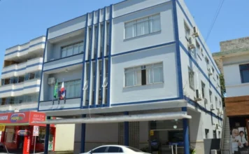 Siderópolis abre processo seletivo para professores e auxiliares Edifício de cor azul e branca no centro de Siderópolis, sede da administração municipal que realiza o processo seletivo.