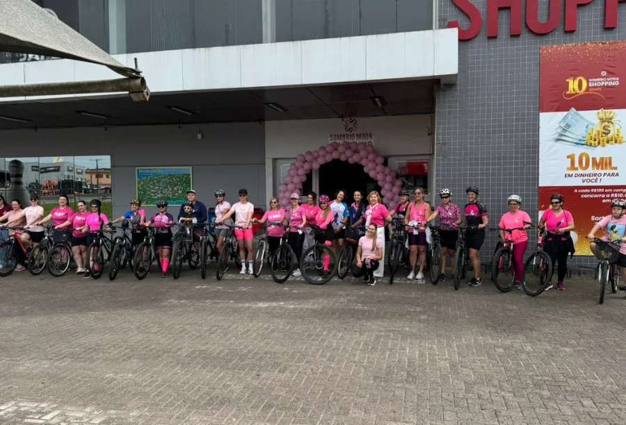 Sombrio Moda Shopping realiza “Pedal Rosas Sobre Rodas” Grande grupo de ciclistas, a maioria mulheres vestindo rosa, em frente ao Sombrio Moda Shopping, reunidas para o evento