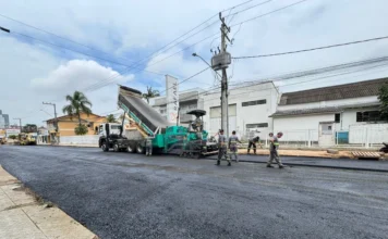 Trânsito no Centro de Araranguá será alterado para obras Caminhão basculante descarregando asfalto em máquina de pavimentação em uma rua do Centro de Araranguá, sinalizando a obra que altera o trânsito.
