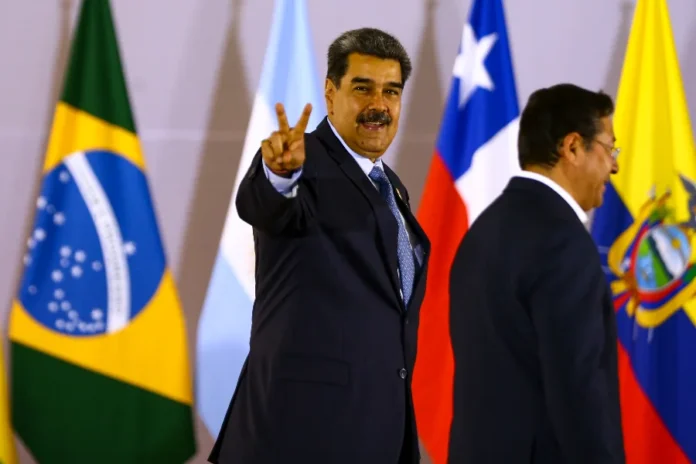 Trump autoriza CIA a realizar operações secretas na Venezuela O presidente da Venezuela, Nicolás Maduro, sorrindo e fazendo o sinal V de vitória com a mão, durante evento internacional, com bandeiras de países como Brasil e Chile ao fundo.