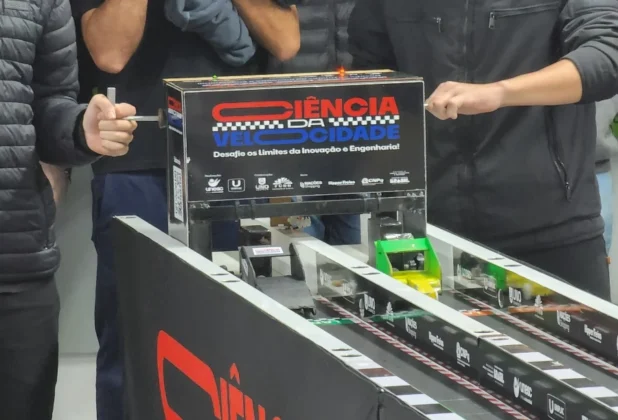 Alunos da UNESC Araranguá lançando protótipos na pista de testes da competição "Ciência da Velocidade", com a logo do evento em destaque.