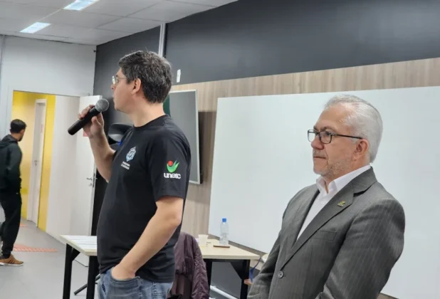 Professor discursando com microfone, com um representante da UNESC Araranguá ao lado, na classificatória do "Ciência da Velocidade".