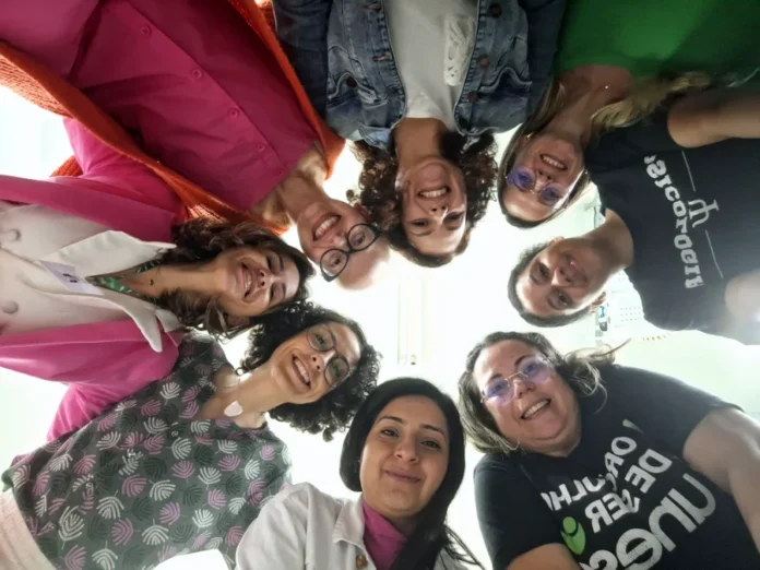 Unesc debate câncer e rompe o silêncio no Outubro Rosa Grupo de mulheres da UNESC e profissionais de saúde, em círculo, sorrindo, em ação de debate e conscientização sobre o câncer no Outubro Rosa em Criciúma.