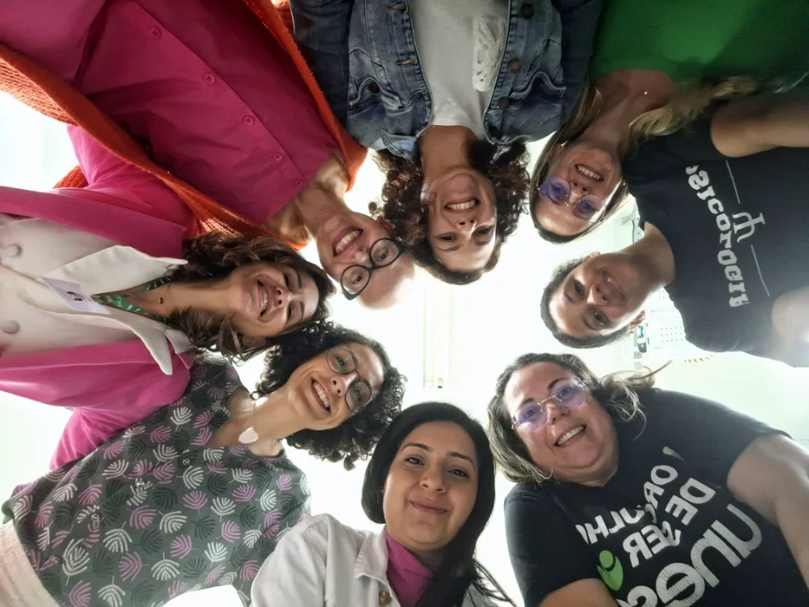 Grupo de mulheres da UNESC e profissionais de saúde, em círculo, sorrindo, em ação de debate e conscientização sobre o câncer no Outubro Rosa em Criciúma.
