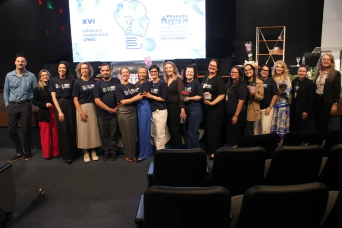 Unesc encerra SCT 2025 com 2,8 mil envolvidos e balanço positivo Equipe de organizadores e professores da UNESC posando para foto no palco, celebrando o encerramento da 16ª Semana de Ciência e Tecnologia (SCT), que envolveu 2,8 mil pessoas em Criciúma.