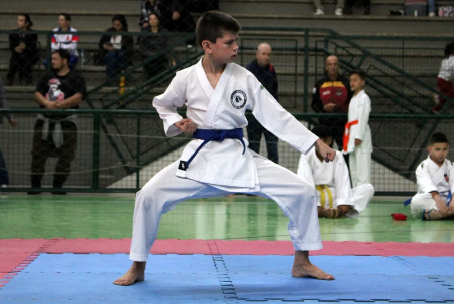 Jovem atleta em quimono branco com faixa azul, executando um golpe (kata) durante a Copa Criciúma de Karatê sediada pela UNESC.