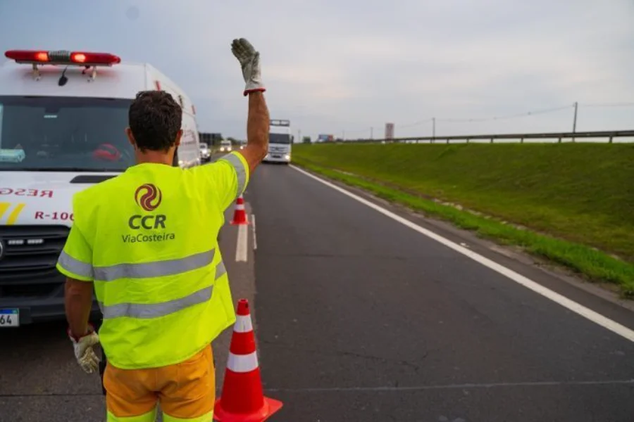 Vagas de Verão ViaCosteira contrata para praças de pedágio Funcionário da CCR ViaCosteira com colete refletivo amarelo, orientando o trânsito na BR-101, em contexto de vagas de emprego para a alta temporada.