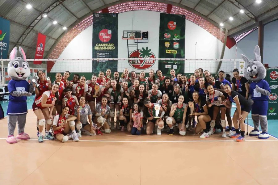 Equipe de vôlei feminino de Criciúma e mascotes em quadra, com jogadoras segurando medalhas de prata após conquistarem o vice-campeonato Brasileiro Sub-19.