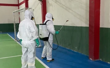 Araranguá intensifica combate à dengue com altas temperaturas Agentes de saúde em macacões brancos e máscaras, realizando a Borrifação Residual Intradomiciliar (BRI) de inseticida em uma quadra esportiva, como parte da intensificação do combate à dengue em Araranguá.