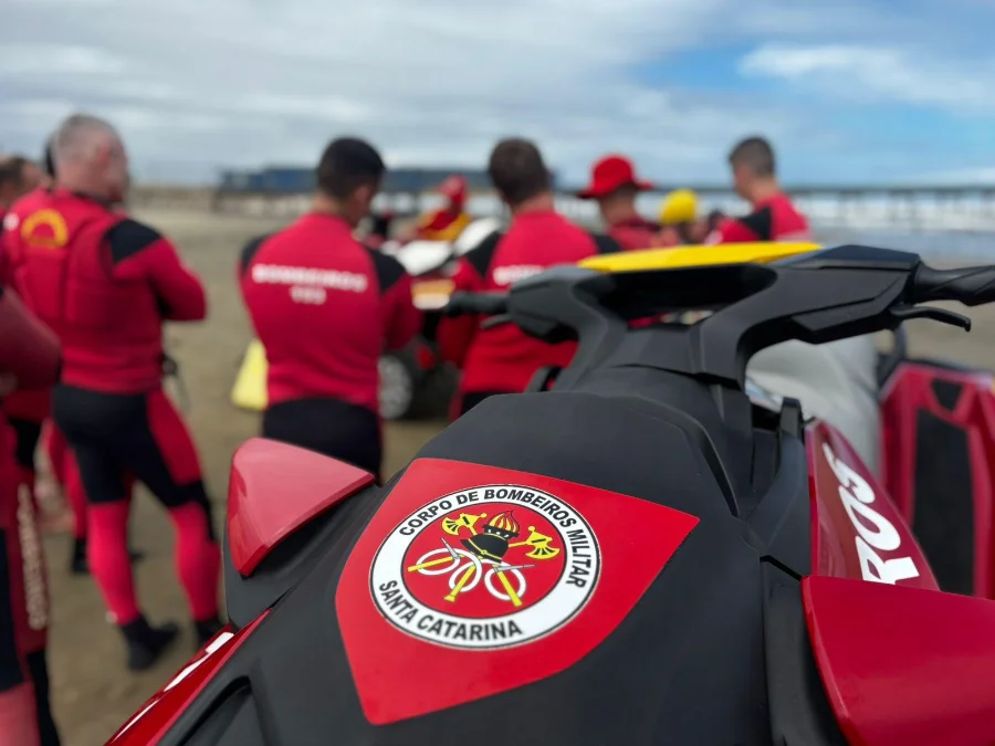 Bombeiros iniciam pré-temporada de verão no Litoral Sul Detalhe da parte traseira de um jet ski de resgate do Corpo de Bombeiros Militar de Santa Catarina (CBMSC) com o emblema em destaque, com guarda-vidas em uniformes vermelhos reunidos na areia, marcando o início da pré-temporada da Operação Estação Verão no Litoral Sul.