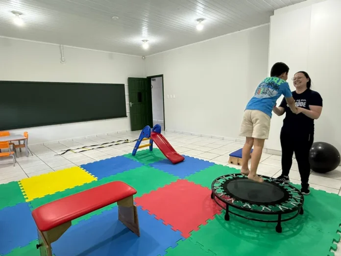 Cocal do Sul inicia grupo de apoio para pais de autistas Criança pulando em trampolim terapêutico, auxiliada por uma terapeuta, em sala com tatames coloridos no novo Centro Terapêutico de Cocal do Sul, que oferece atendimento a pacientes com transtornos do neurodesenvolvimento.